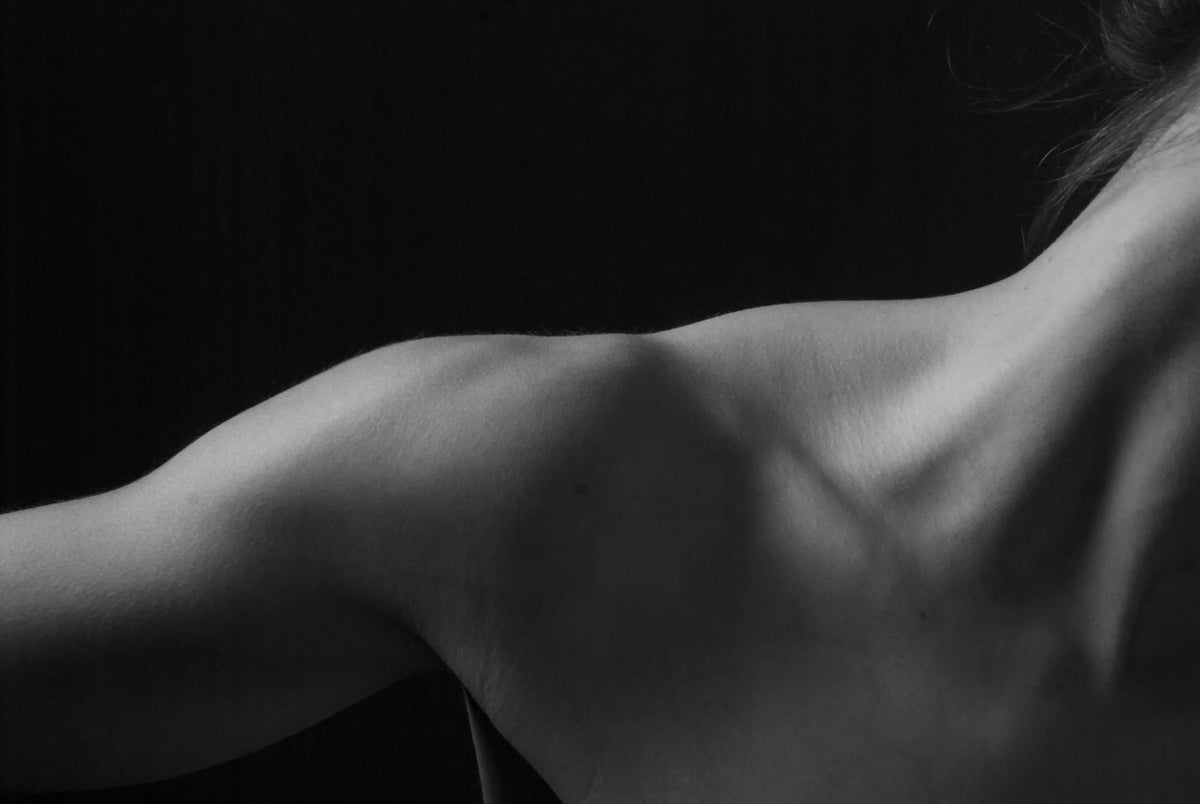 A woman's bare shoulder and back in soft light, in black and white